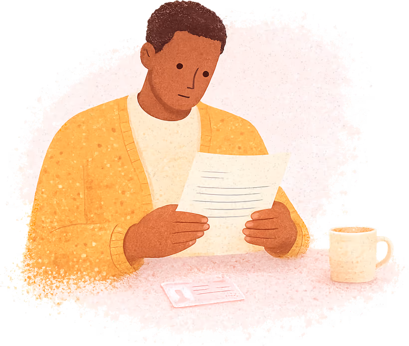 A man with a short afro in a mustard cardigan sitting at a kitchen table, reading a letter held in both hands, with a driving licence card and a mug on the table in front of him